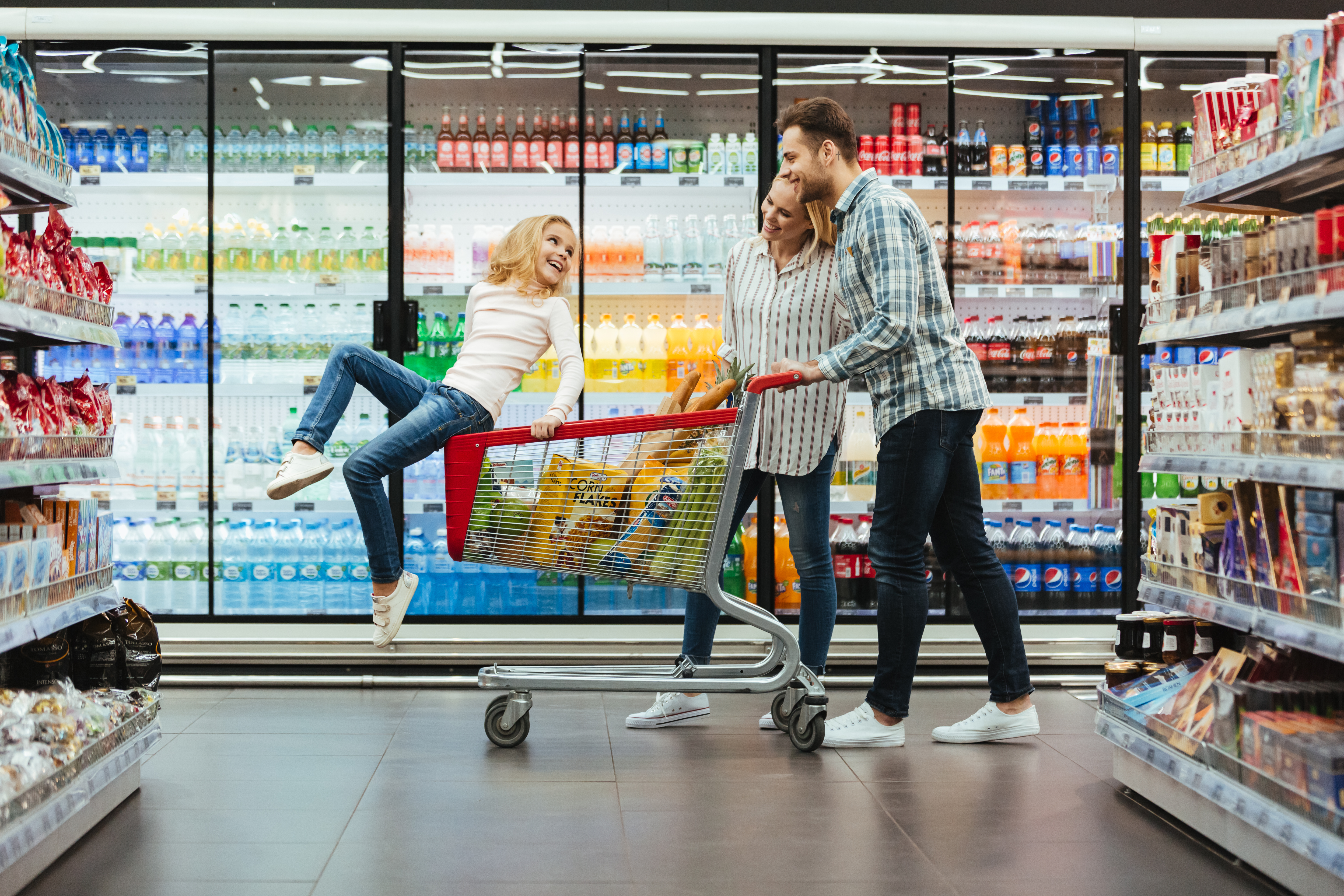 Cheerful young family with a child sitting on a cart walking at the supermarket